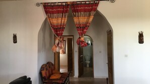 Une pièce comprenant un canapé, un fauteuil et un banc en bois. Deux portes donnent accès à d’autres pièces.