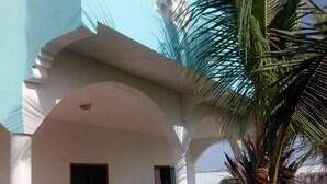 Un bâtiment à la façade bleu clair, doté d’un patio couvert avec des chaises et des tables, et d’un palmier.