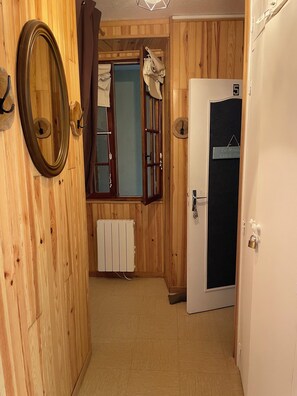 Un couloir en bois avec un radiateur, une porte portant une plaque de numéro et un miroir.