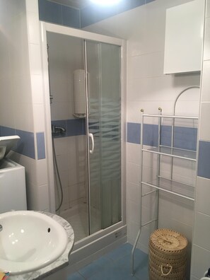 Une salle de bain avec une douche à parois de verre, un lavabo blanc, un porte-serviettes et un petit panier en osier.
