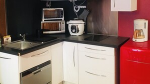 Eine kompakte Küche mit weißen Schränken, einer Mikrowelle, einem Slow Cooker, einer Kaffeemaschine und einem Geschirrspüler.