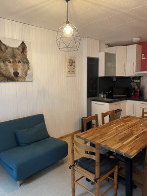 A modern kitchen with white cabinets, a wooden dining table, and a blue sofa.