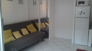 A modern living room with a grey sofa, yellow cushions, a white refrigerator, and a microwave.