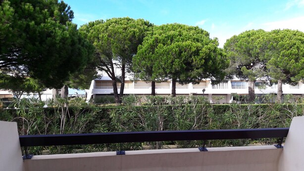 A balcony with a railing overlooking a landscaped area with trees and a building in the background.