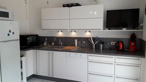 A modern kitchen with white cabinets, a black microwave, a sink with a cutting board, and a red coffee maker.