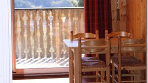 A wooden interior with a dining table and chairs, a window with a view of a landscape, and a red curtain. - SPACIOUS STUDIO 30M2 balcony south facing terrace 4 pers near downtown (Barcelonnette)