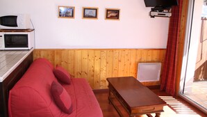 A room with a wooden wall, a red sofa, a small wooden table, a TV mounted on the wall, and a window with curtains. - SPACIOUS STUDIO 30M2 balcony south facing terrace 4 pers near downtown (Barcelonnette)