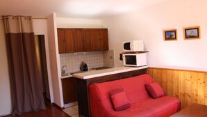 A compact living space with a kitchenette, a red sofa, and a wooden panel wall. - SPACIOUS STUDIO 30M2 balcony south facing terrace 4 pers near downtown (Barcelonnette)