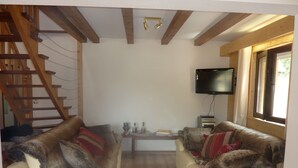 A living room with two sofas, a TV, a wooden staircase, and a window.