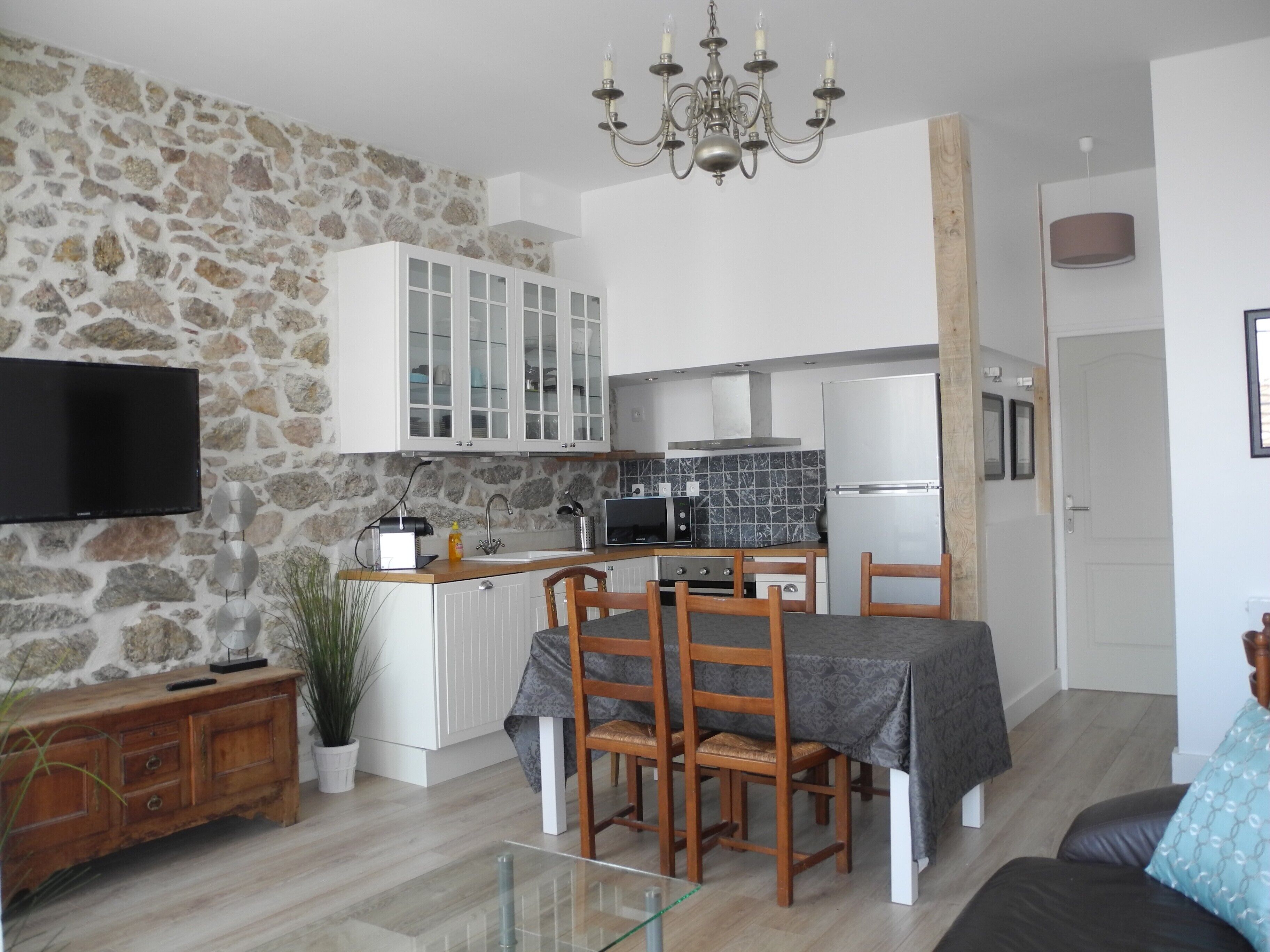 A modern kitchen with white cabinets, a built-in oven, and a microwave. There is a dining table with chairs and a TV mounted on the wall.