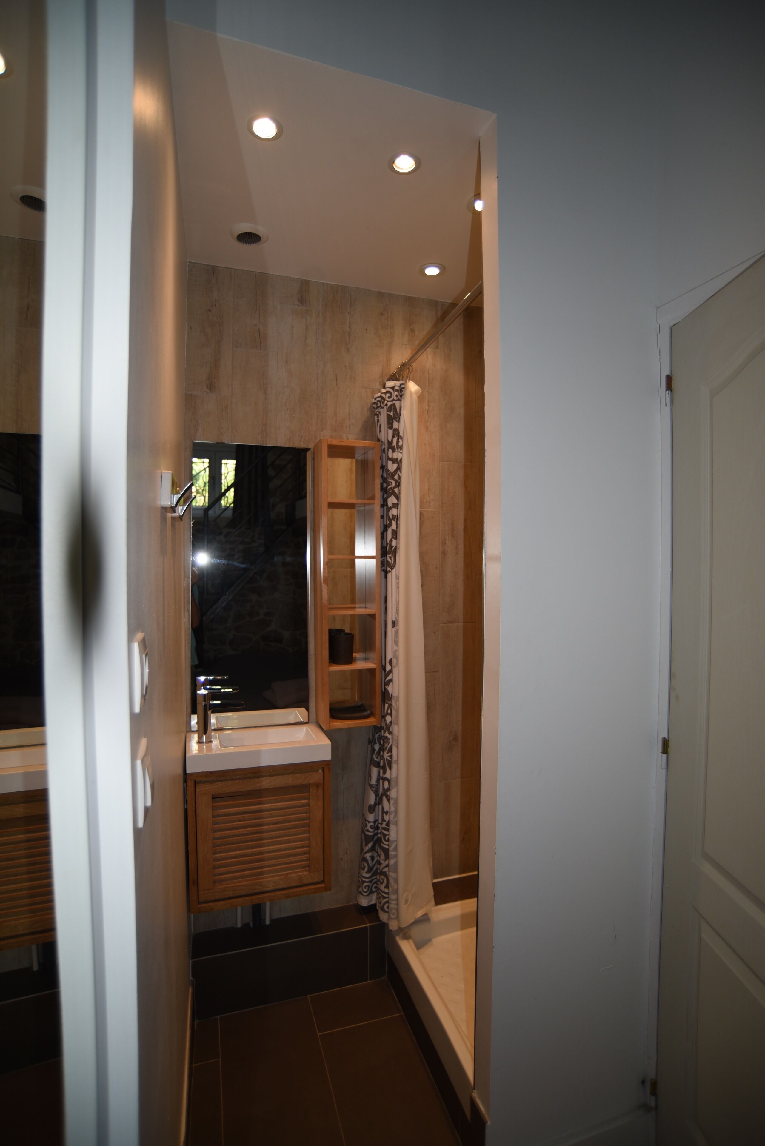 A modern bathroom with a glass shower enclosure, a wooden vanity, and recessed ceiling lighting.