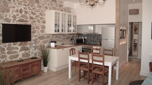 Uma cozinha moderna com paredes de pedra, armários brancos, forno embutido e uma área de jantar com cadeiras de madeira.