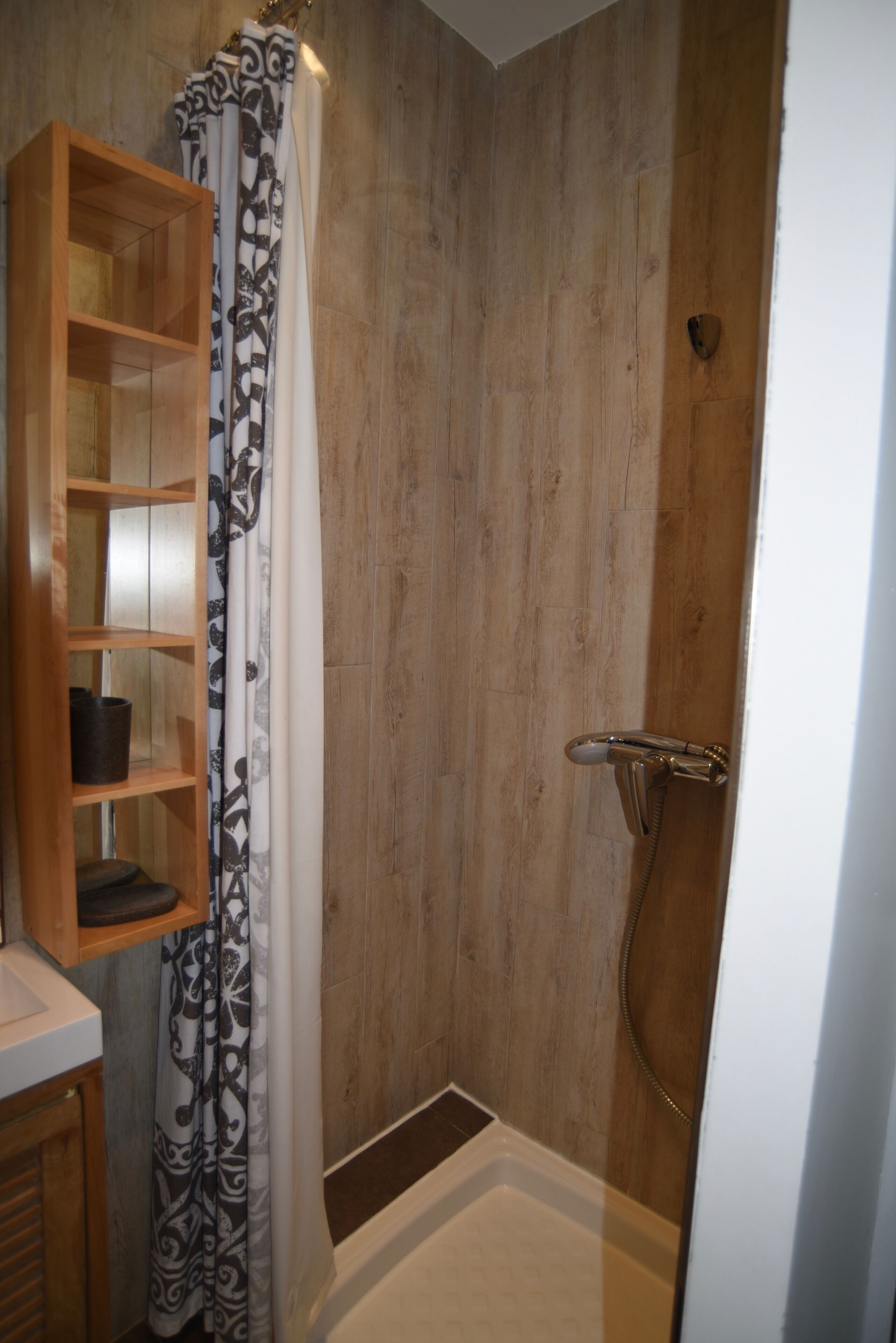 A shower with a wooden door, a shower curtain, and a shelf with a black container.