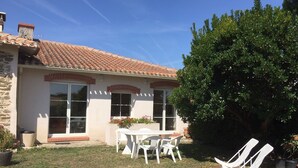 Una casa con techo de tejas, un patio con mesa y sillas, y un árbol grande en el jardín trasero.