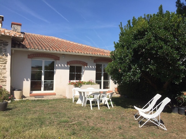 A house with a tiled roof, a patio with a table and chairs, and a large tree in the backyard.