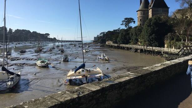 Un muelle de piedra con barcos amarrados, un puente de madera y una torre histórica al fondo.