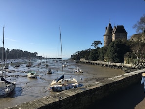 A waterfront with boats docked along a stone quay, a wooden bridge, and a historic tower in the background.