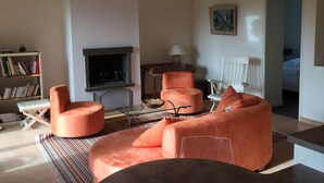 Una sala de estar con chimenea, muebles naranja, una estantería y un cuadro en la pared.