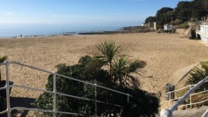 Una playa con una escalera que baja hacia la orilla, rodeada de vegetación y con vistas al mar.
