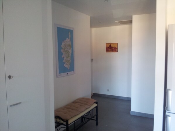 A hallway with a bench, two framed artworks on the walls, and a door on the left. - NEW 2-ROOM APARTMENT WITH SEA VIEW (Propriano)