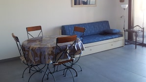 Et spiseområde med et rundt bord, fire stole, en blå sofa og et billede i ramme på væggen.