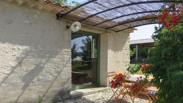 Un bâtiment en pierre avec une porte verte et un petit patio comprenant une table et des chaises.