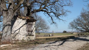 Un bâtiment rustique en pierre, doté d’un toit en pente, entouré d’arbres et bordé d’un chemin de gravier.