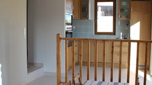 Un espace repas avec une table et des chaises en bois, un escalier menant à un niveau supérieur et une cuisine à l’arrière-plan.
