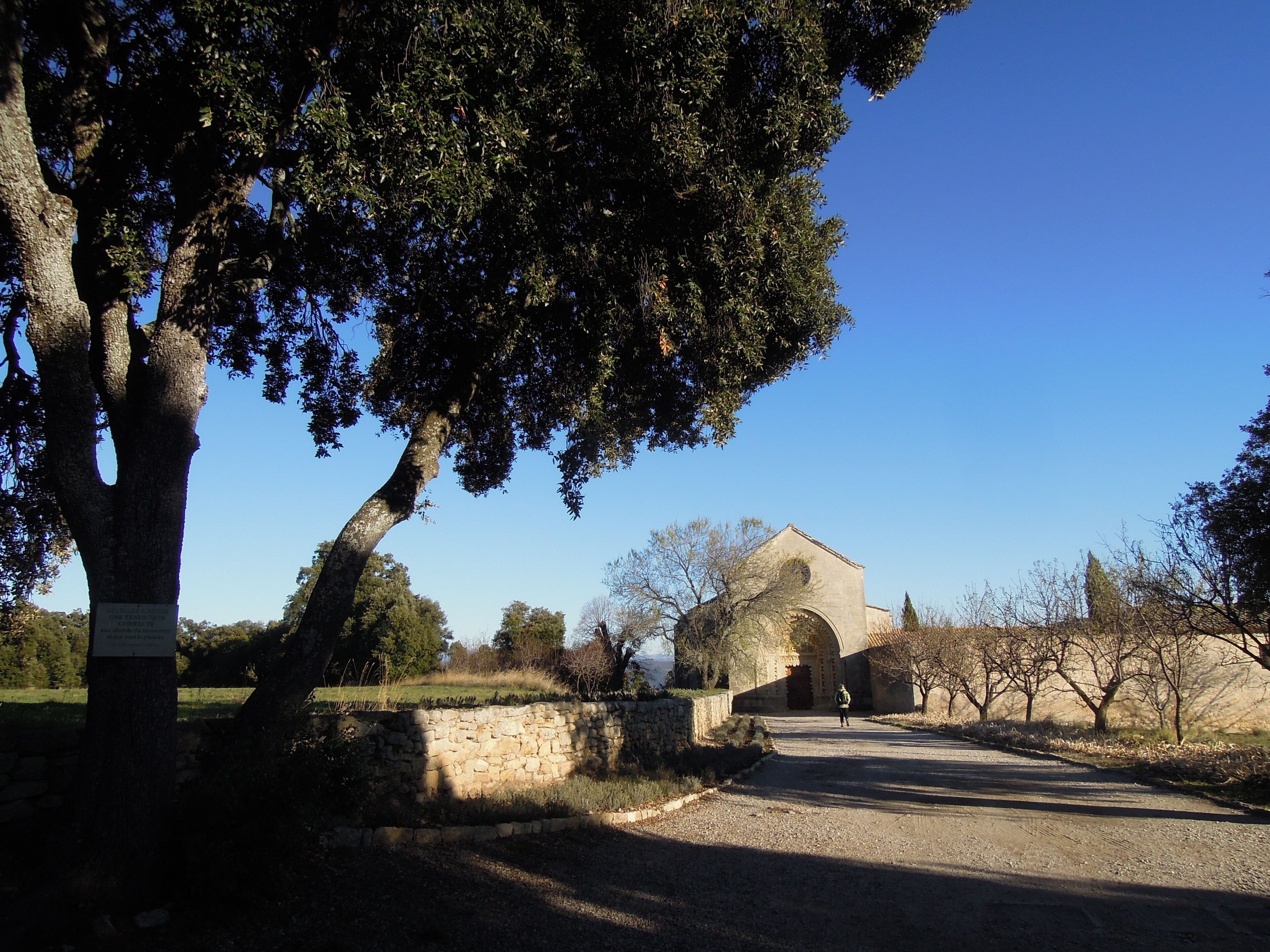 A rural road leading to a stone building with an arched entrance, surrounded by trees and a stone wall.