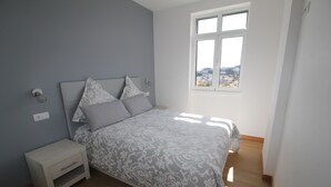 A bedroom with a bed, nightstand, and a window with a city view. - Fully renovated apartment, in the Centre of Funchal. AMAZING view (Funchal)