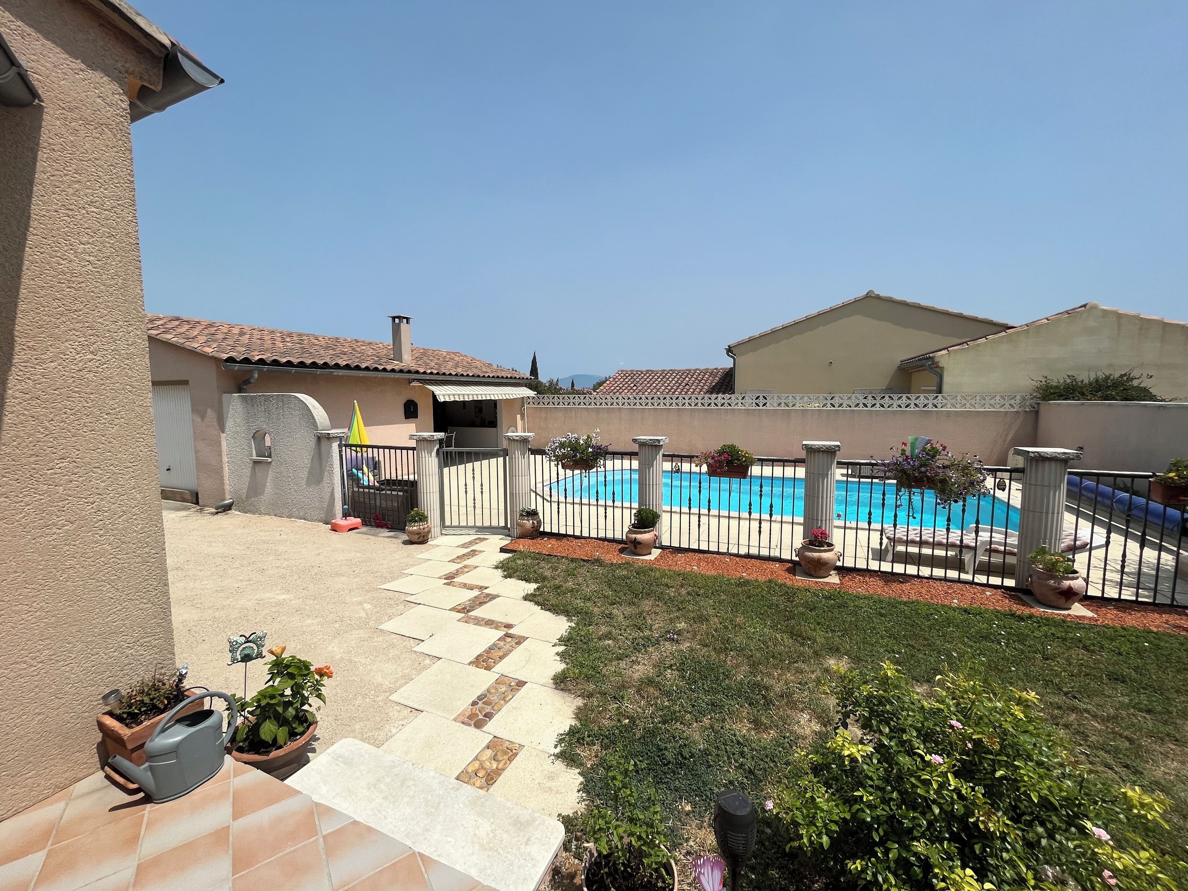 A residential property with a swimming pool, a patio with potted plants, and a clear sky.