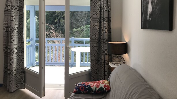 A room with a sliding glass door leading to an outdoor balcony, a sofa with a colorful pillow, a wall-mounted lamp, and a framed picture.