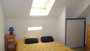 A bedroom with a skylight, a bed with two pillows, a nightstand with a lamp, and a wardrobe.