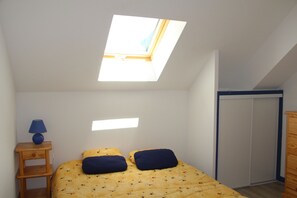 Un dormitorio con tragaluz, una cama con dos almohadas, una mesita de noche con lámpara y un armario.