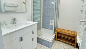 A modern bathroom with a white vanity, a glass shower enclosure, and a wooden bench.