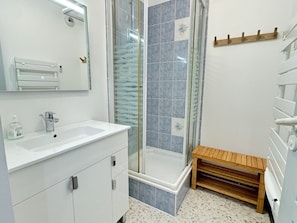 Un baño moderno con un tocador blanco, una cabina de ducha de vidrio y un banco de madera.