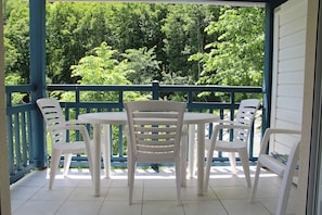 Un espacio de estar al aire libre techado con una mesa y sillas, con vista a un área boscosa.