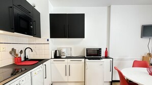 A compact kitchen with a washing machine, a microwave, a coffee maker, and a small refrigerator.