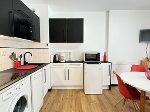 Una cocina compacta equipada con lavadora, microondas, cafetera y un refrigerador pequeño.