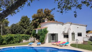 Une piscine avec des chaises longues et un bâtiment blanc doté d’un toit en tuiles.