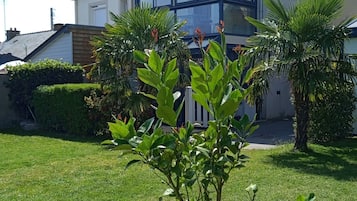 Une maison moderne à deux étages, dotée d’une grande baie vitrée au rez-de-chaussée, entourée d’une pelouse bien entretenue et de quelques petits arbres.