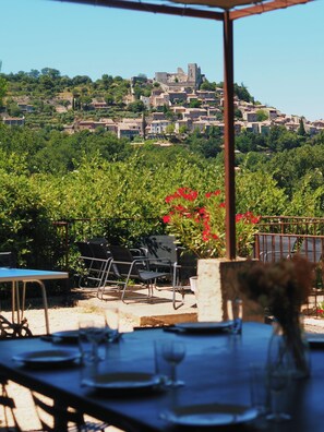 An outdoor dining area with tables and chairs, overlooking a hillside with buildings and greenery.