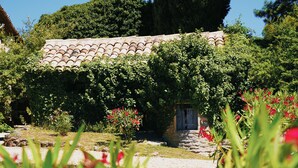 Ein traditionelles Steinhaus mit Ziegeldach, umgeben von üppigem Grün und blühenden Pflanzen.