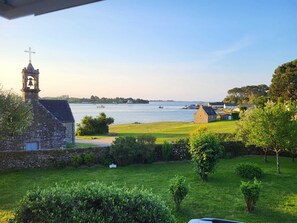A stone building with a bell tower, a grassy area, and a view of the water with boats. - Charming villa in Saint-Philibert (close to Carnac) directly by the sea. 3*rated (Saint-Philibert)