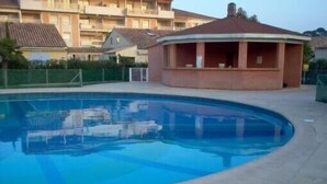 A swimming pool with a circular structure nearby, surrounded by a fence and residential buildings in the background. - Maset conditioning in a closed condominium with guardian. (Le Lavandou)