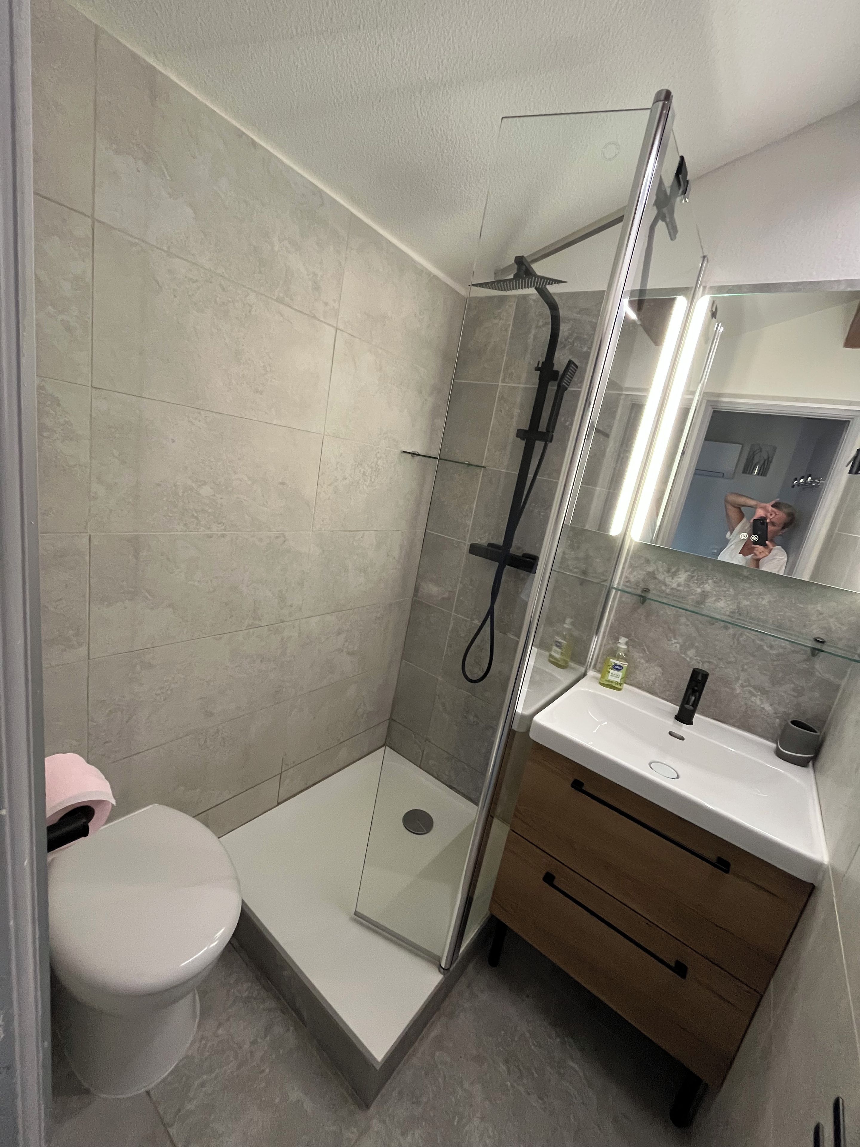 A modern bathroom with a glass-enclosed shower, a white toilet, and a vanity with a mirror.