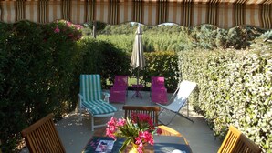 An outdoor patio with striped ceiling, a table with a vase of flowers, and several chairs. - Maset conditioning in a closed condominium with guardian. (Le Lavandou)
