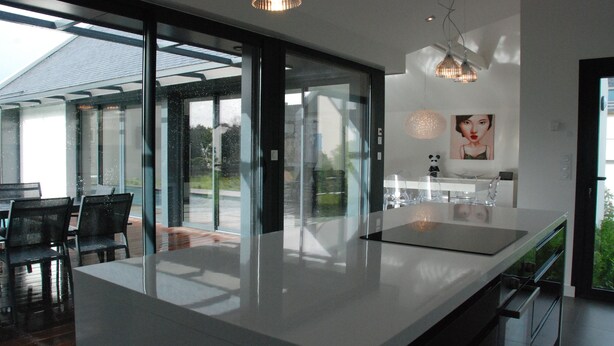 A modern kitchen with a large island, glass doors leading to a patio, and contemporary lighting fixtures. - Magnificent villa with heated pool close to beaches (Arzon)