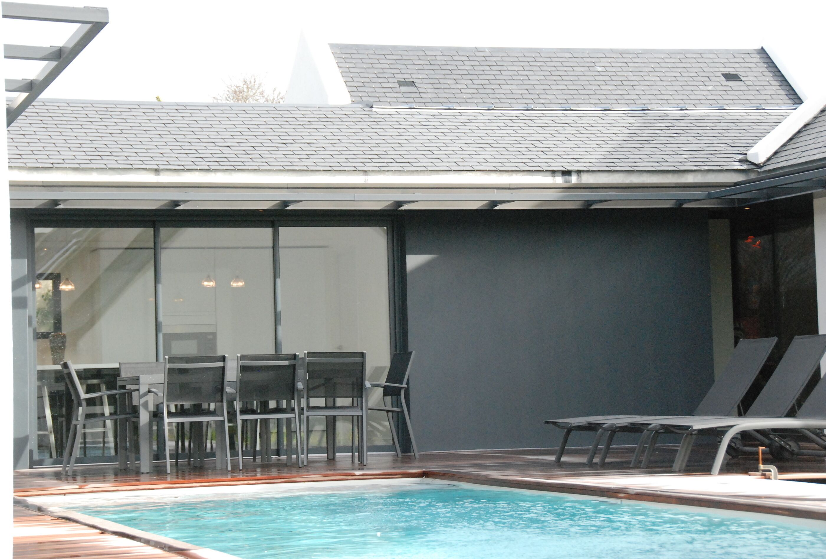 Una piscina con sillones de descanso y una zona de estar cubierta.