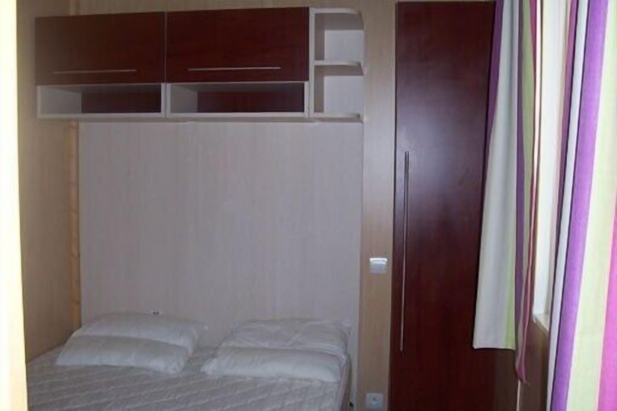 A bedroom with a bed, wooden wardrobe, and a curtain.